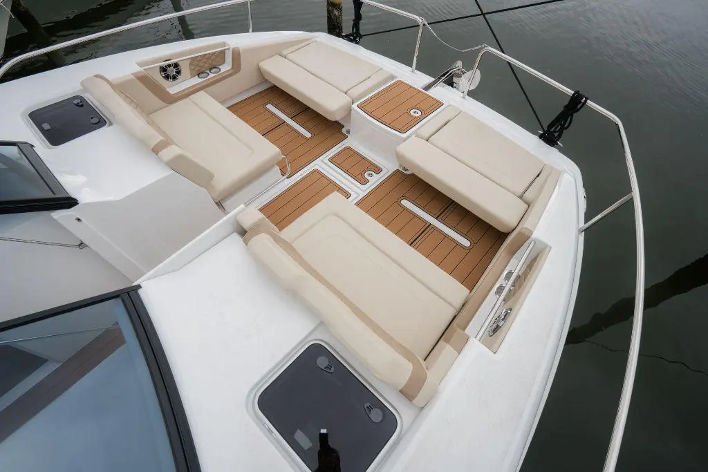 Spacious boat deck with cream seating, teak accents, and control panel, overlooking calm water reflections.